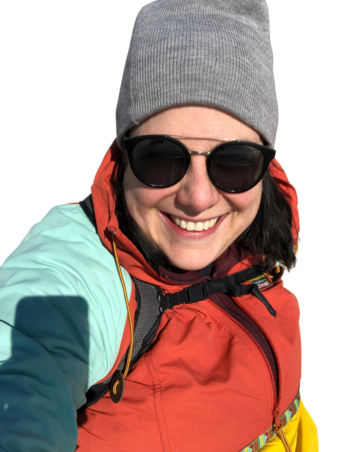 A smiling mid-fat white woman wearing a colourful anorak, grey toque, and sunglasses. 
